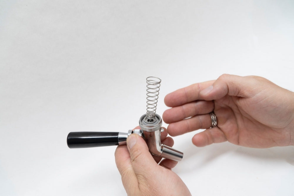 En person monterer en Keg King Ultratap Twist Selvlukkende Fjær gjennomstrømningsventil i metall med svart håndtak og synlig automatisk lukkefjær mot en hvit bakgrunn.