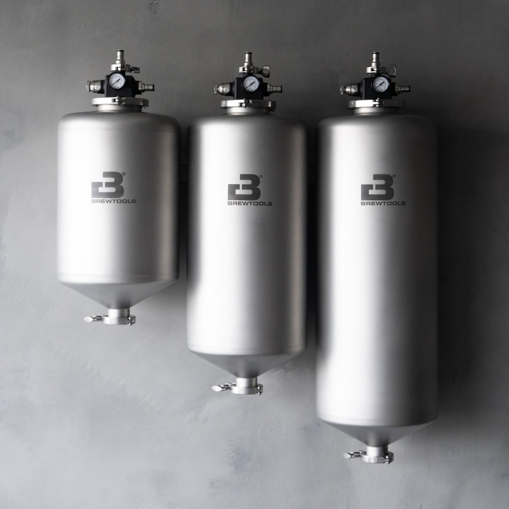 Tre Brewtools MiniUni 50-fermentorer fra Brewtools er montert på en grå vegg, hver utstyrt med standardtilbehør som ventiler og trykkmålere for presis trykkfermentering.