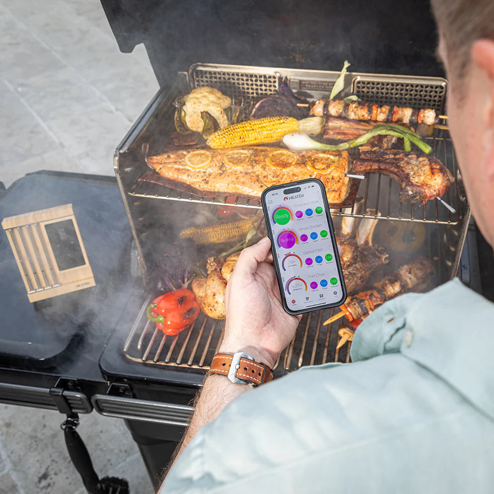 En person griller kjøtt og grønnsaker mens han eller hun overvåker dem med Traeger Meater Pro XL - WiFi-steketermometer, og bruker smarttelefonappen til å holde oversikt over temperatur og tilberedning.