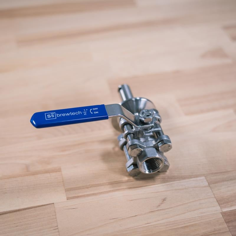 En 1,5" Tri-Clamp Whirlpool Fitting fra Ss Brewtech med blått håndtak og On/Off-merking er plassert på en lys treflate.