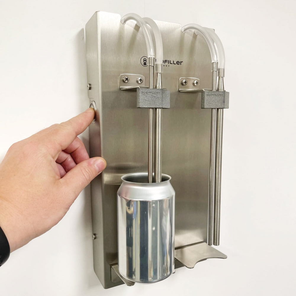En hånd trykker på en knapp på Duofiller Core (G3) Automatic Can Filler fra Duofiller, med en aluminiumsboks plassert under de to påfyllingsmunnstykkene.