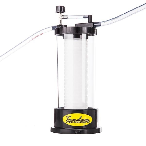 En klar plastbeholder merket Tenco, som inneholder en 1 mikron filterpatron for Enolmatic Tandem Filter Housing, med svart bunn og lokk, gjennomsiktige innløps- og utløpsrør; næringsmiddelgodkjent for sikker bruk.
