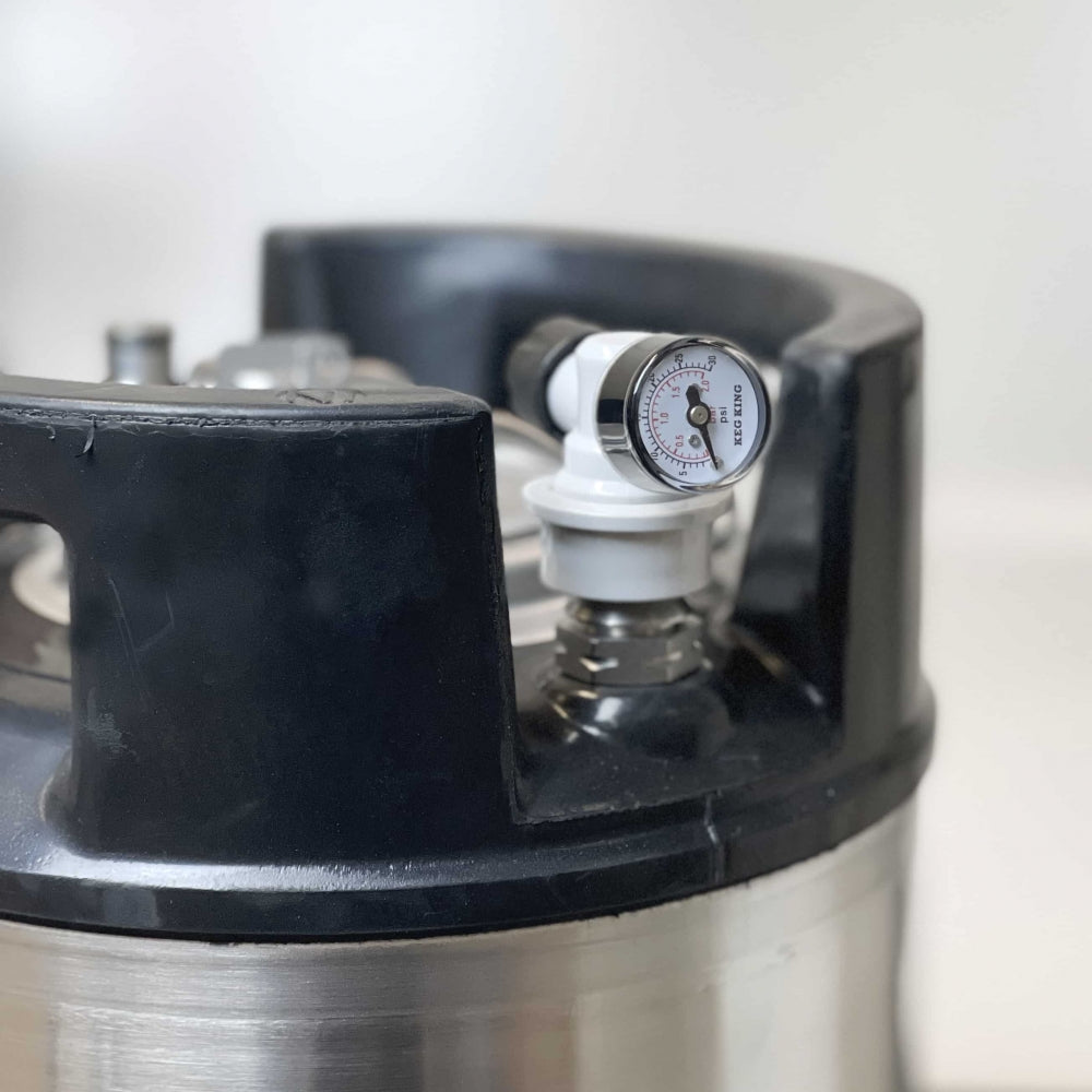 Nærbilde av et Keg King-fat i rustfritt stål med Spundy - Compact Spunding Valve fra Keg King og tilhørende trykkmåler, delvis omsluttet av et svart plasthåndtak - perfekt for hjemmebryggingsentusiaster.
