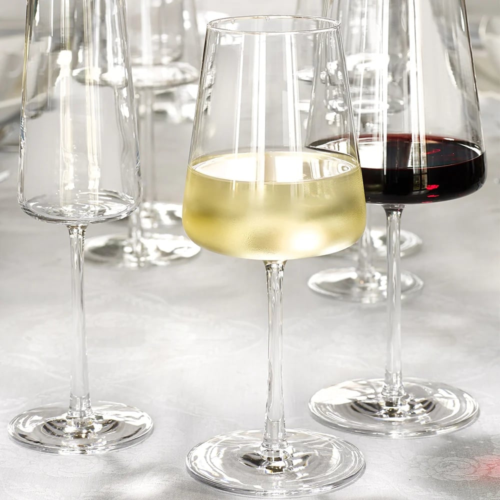 A POWER White Wine vinglass 400ml fra Stölzle Lausits, fylt med hvitvin, står ved siden av et glass rødvin og to tomme krystallglass på et lyst bord.