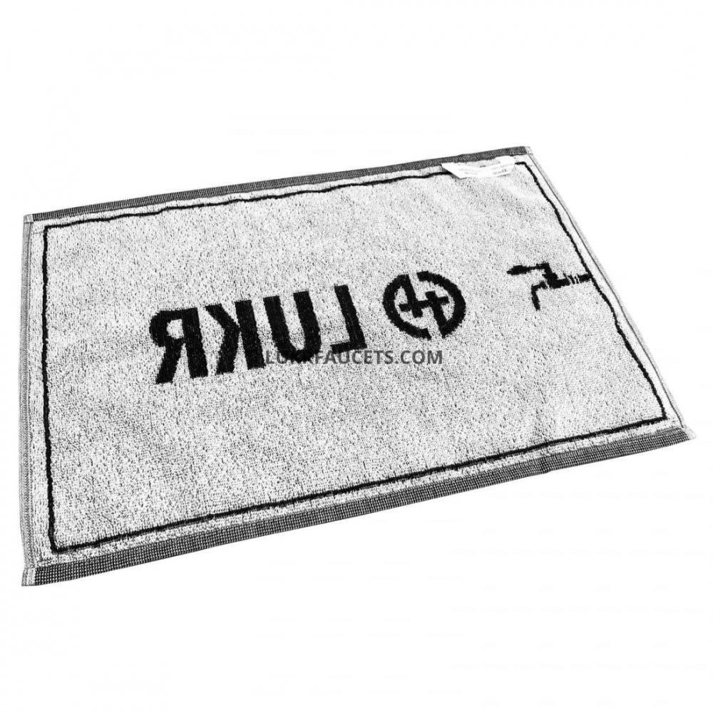 Lukr Bar Towel er en hvit rektangulær bomullsdørmatte på 50x30 cm med en svart kant, ordet "LUKR" trykt bakover i svart og en krangrafikk - designet for å se ut som et stilig barhåndkle.