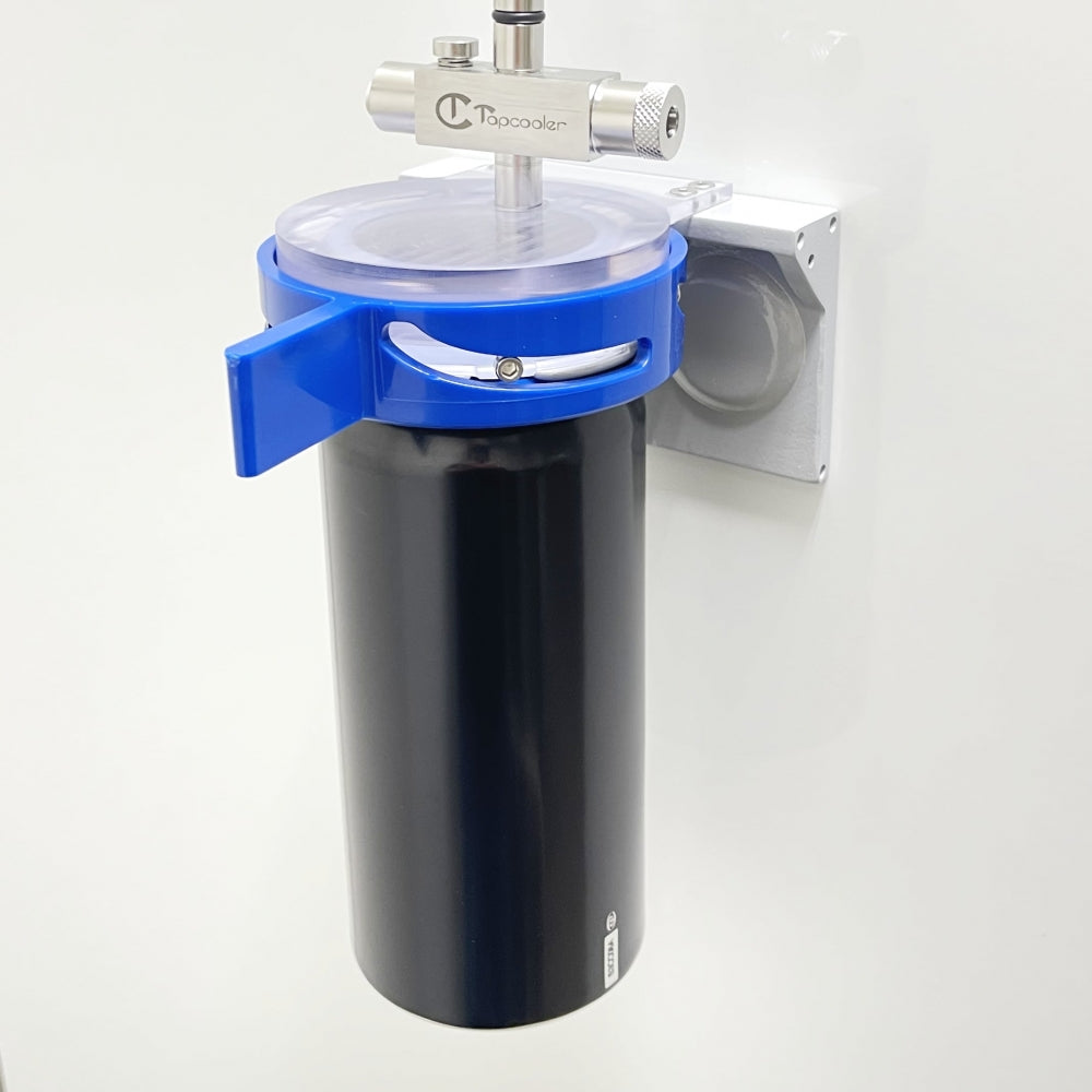 Et svart og blått vannfilterhus er montert på en hvit vegg med en metallventil og et metallrør på toppen, i likhet med oppsett for tapping av rene drikkevarer ved hjelp av Tapcooler Nanocanner IM - Boksfyller fra Tapcooler.