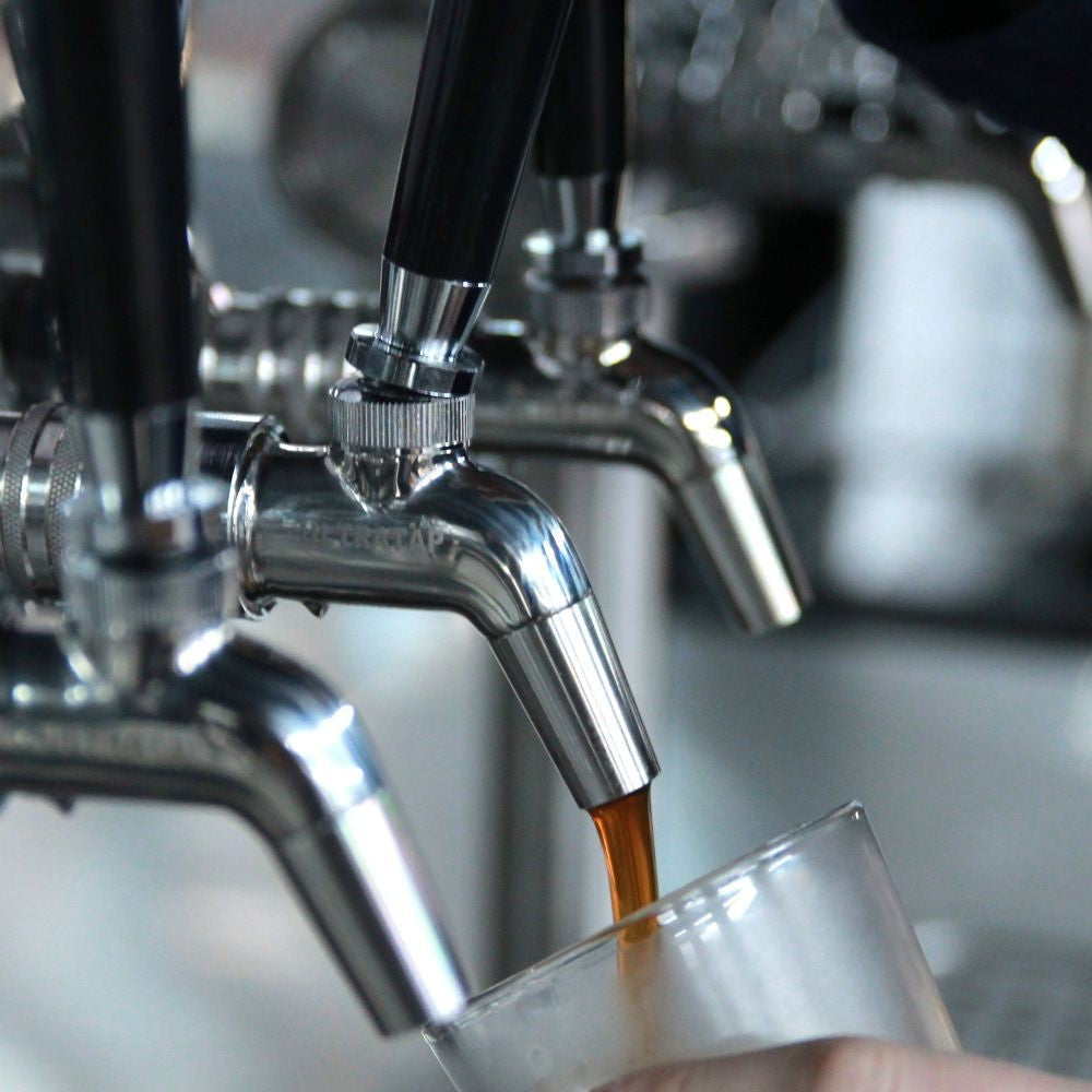 En drikk helles fra en Keg King Ultratap SS tappekran - med håndtak over i en klar kopp, mens flere kraner er synlige i bakgrunnen.