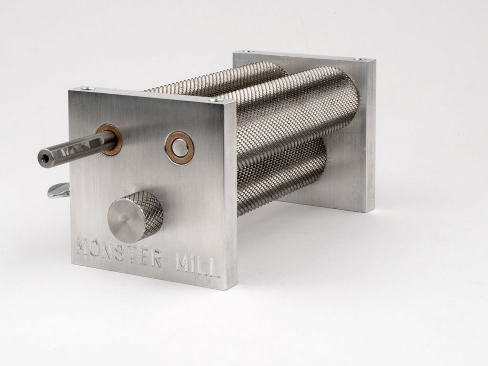 Monster Brewing Hardware Monster Mill MM-3, med en solid base, beholder og tre teksturerte valser for hjemmebrygging, har en enkel hvit bakgrunn med varemerket inngravert på frontplaten.