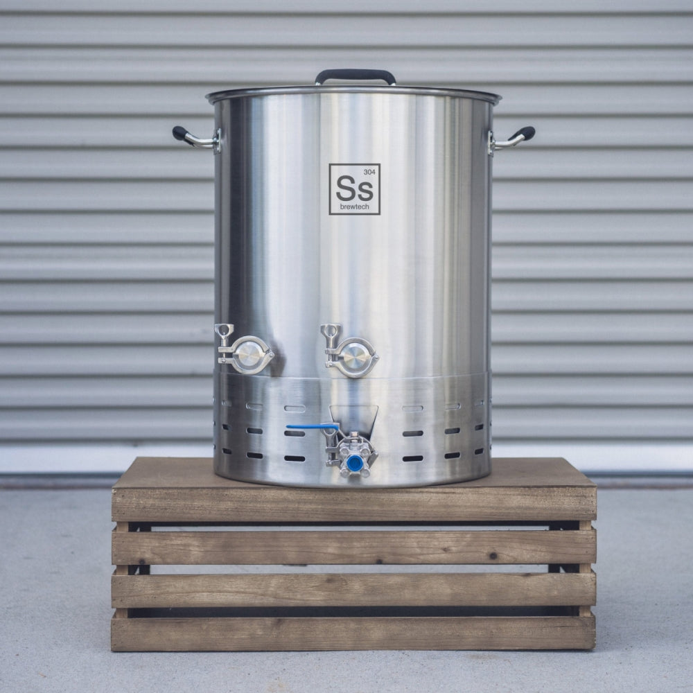 Ss Brewtech Brewmaster Edition Kettle 75 l (20 gal) Bryggekjele, en stor bryggekjele i rustfritt stål med to ventiler fra Ss Brewtech, står på en trekasse foran en metallskodde.