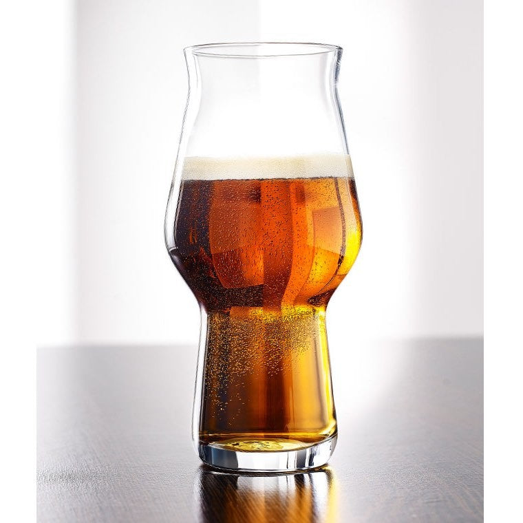 Et tulipanformet Rastal Craft Master One 47 cl ølglass, fylt med ravfarget øl kronet med skum, hviler på en mørk treflate mot en lys bakgrunn.