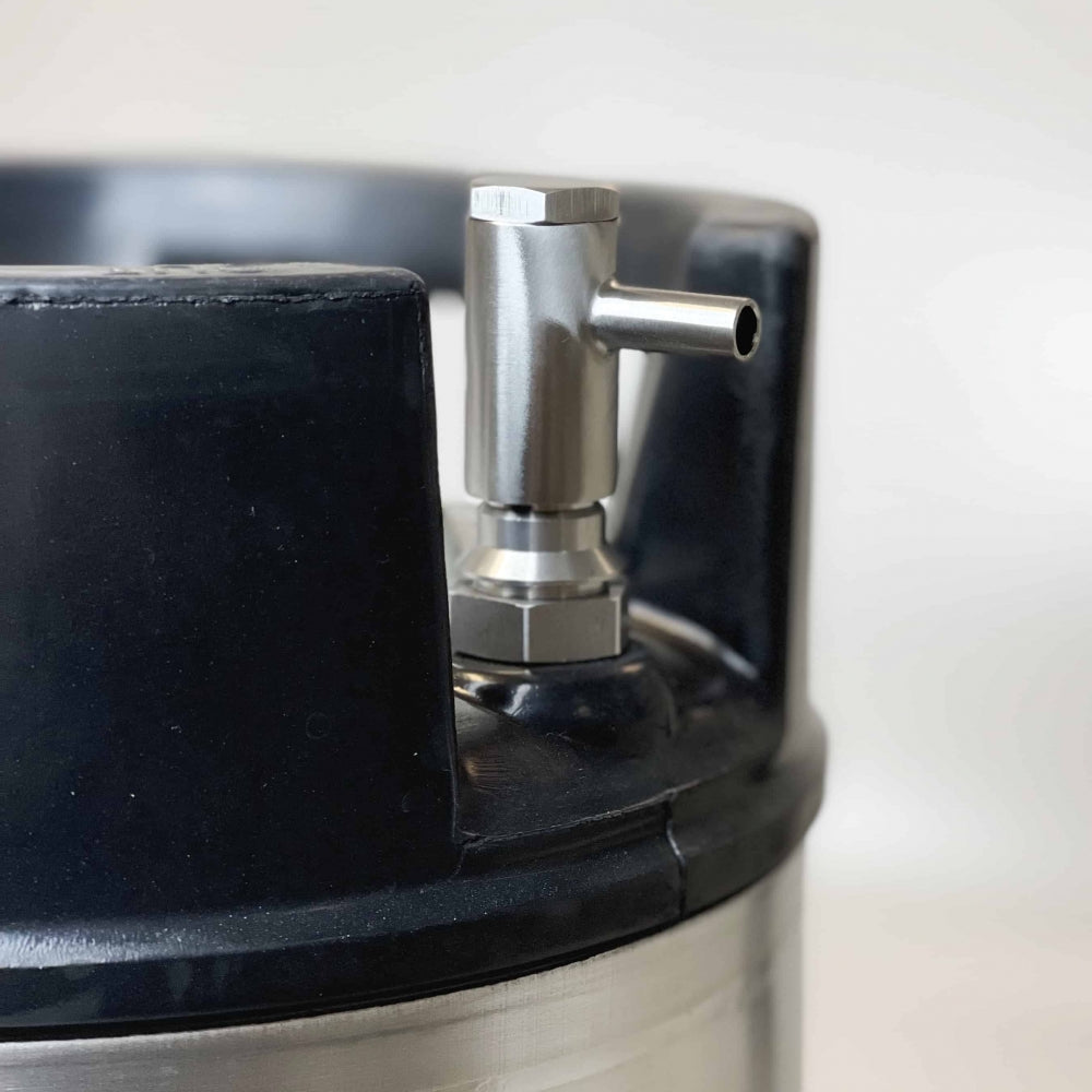 Nærbilde av Keg King Quickie - Cornelius Post Dispenser på et fat i rustfritt stål, med svart plasthåndtak, ventilbeslag i metall og kompatibilitet med ventiltilkoblinger med kulelås.