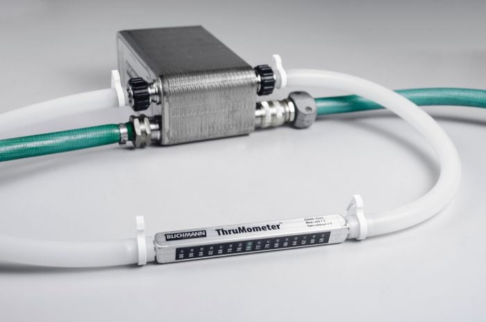 Et Blichmann ThruMometer 3/8" inline-termometer fra Blichmann kobler sammen en metallvarmeveksler og en grønn slange med 3/8" rør på en ren overflate.