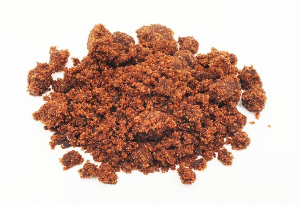 En haug med Brewolution Muscovado sukker 1 kg granulat og klumper på en hvit bakgrunn fremhever den rike fargen og konsistensen til dette uraffinerte søtningsmiddelet.