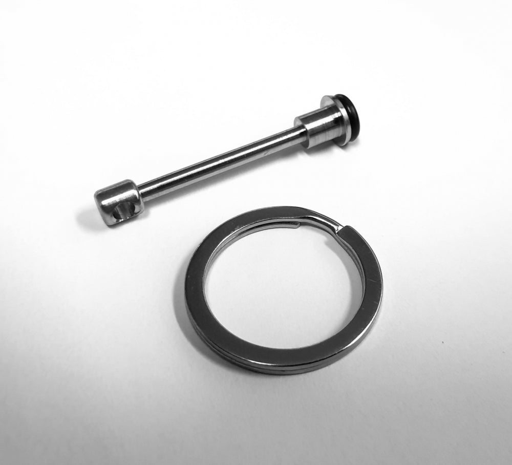En Tapcooler manuell trykkreduksjon metallstang med gummiring og separat nøkkelring, tilsvarende deler i Tapcooler-systemer, er vist liggende på en hvit flate.