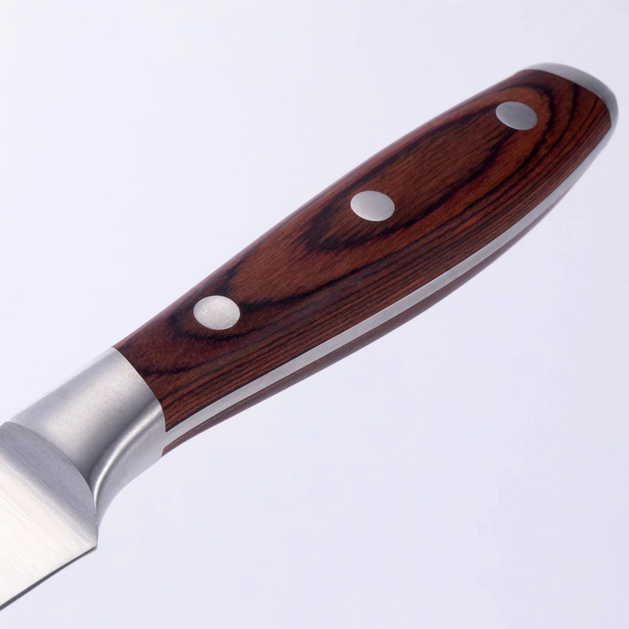 Nærbilde av Avanta Pakkawood Fine Edge Biffkniver-håndtaket fra Messermeister, med trefiberfinish og tre metallnagler, mot en vanlig lys bakgrunn.