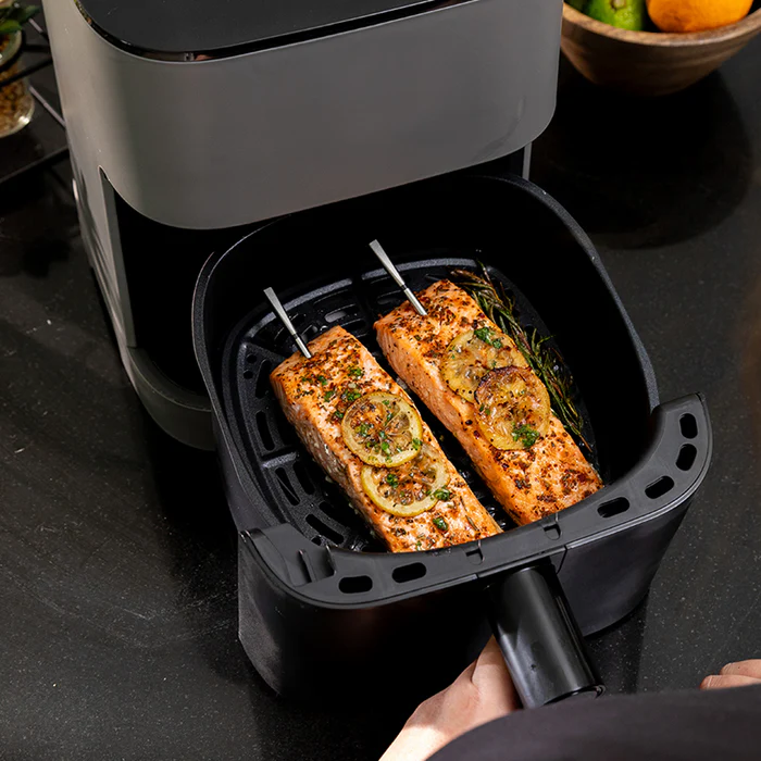 En person holder en frityrgrytekurv med to spiddede laksefileter toppet med sitron og urter, klare til å stekes med Traeger Meater Pro XL - WiFi-steketermometer for perfekte resultater.