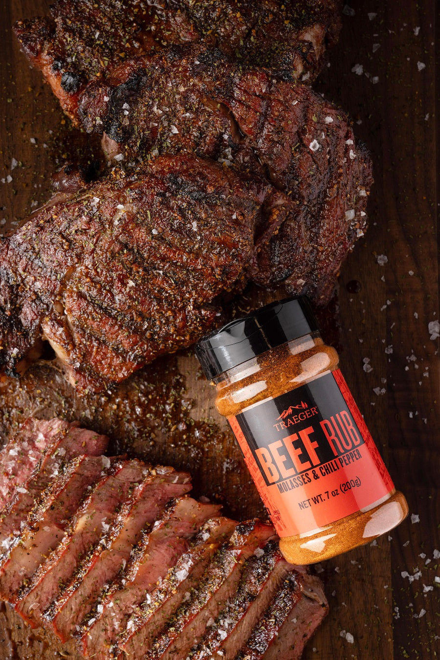 Grillede biffskiver på en treplate, toppet med grovt salt og servert sammen med et glass Traeger Beef Rub 200g fra Traeger.