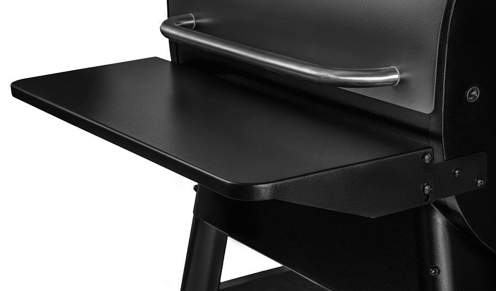 Nærbilde av en Traeger sammenleggbar hylle i svart metall for Pro 575 og Ironwood 650, festet til en grill eller smoker, med et horisontalt håndtak i rustfritt stål over.