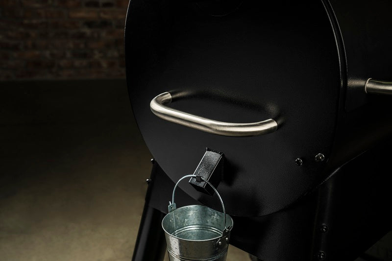 Nærbilde av en Traeger Pro D2 575 pelletsgrill fra Traeger, med metallhåndtak og en liten metallbøtte som henger under askeskuffen.