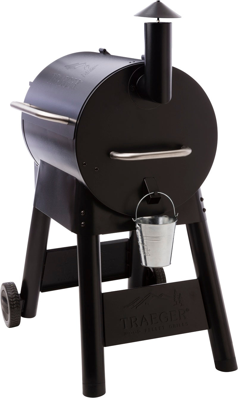 Traeger Pro Series 22 pelletsgrill fra Traeger er svart, har et rundt kammer, skorstein, sidehåndtak, to hjulben og en metallbøtte festet under.