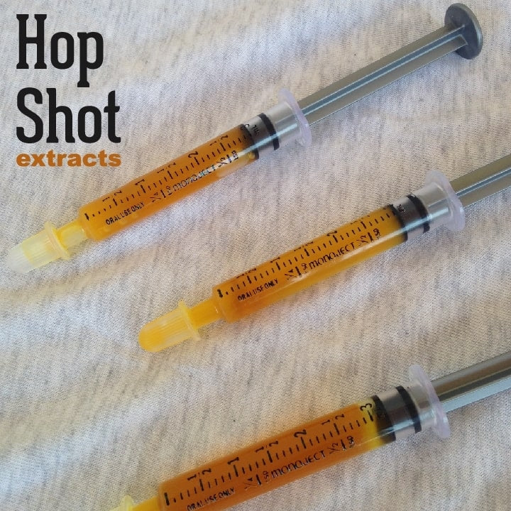 Tre sprøyter med Yakima Valley Hops' Hop Shot 10 ml CO2-humleekstrakt (51,9 %) hviler på et lett stoff, ideelt for presis dosering; "Hop Shot extracts" står øverst til venstre, noe som understreker Brewfather-presisjonen.