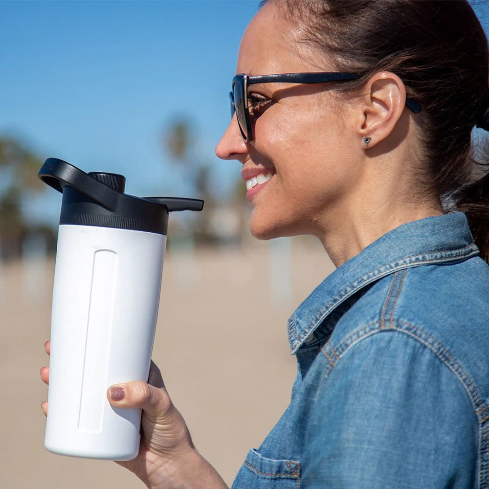 En kvinne i solbriller og denimjakke holder GrowlerWerks uKeg Twist 24 Tungsten (7 dl) Seltzer Maker utendørs på en solrik dag, klar til å nyte nylaget hard selters.