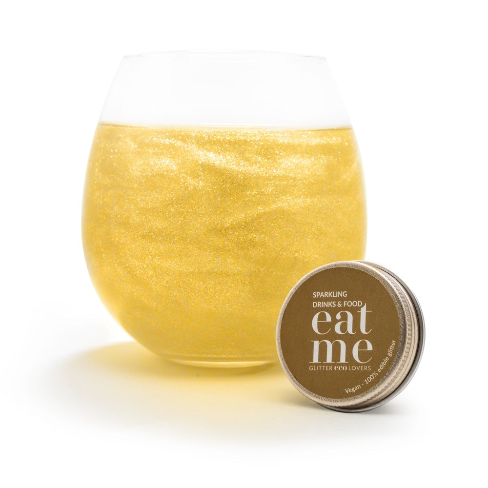 Et rundt glass med en glitrende, gyllen drink sitter bak en liten Eco Lovers Eat Me Glitter Gold 20 ml beholder for mat og drikke.