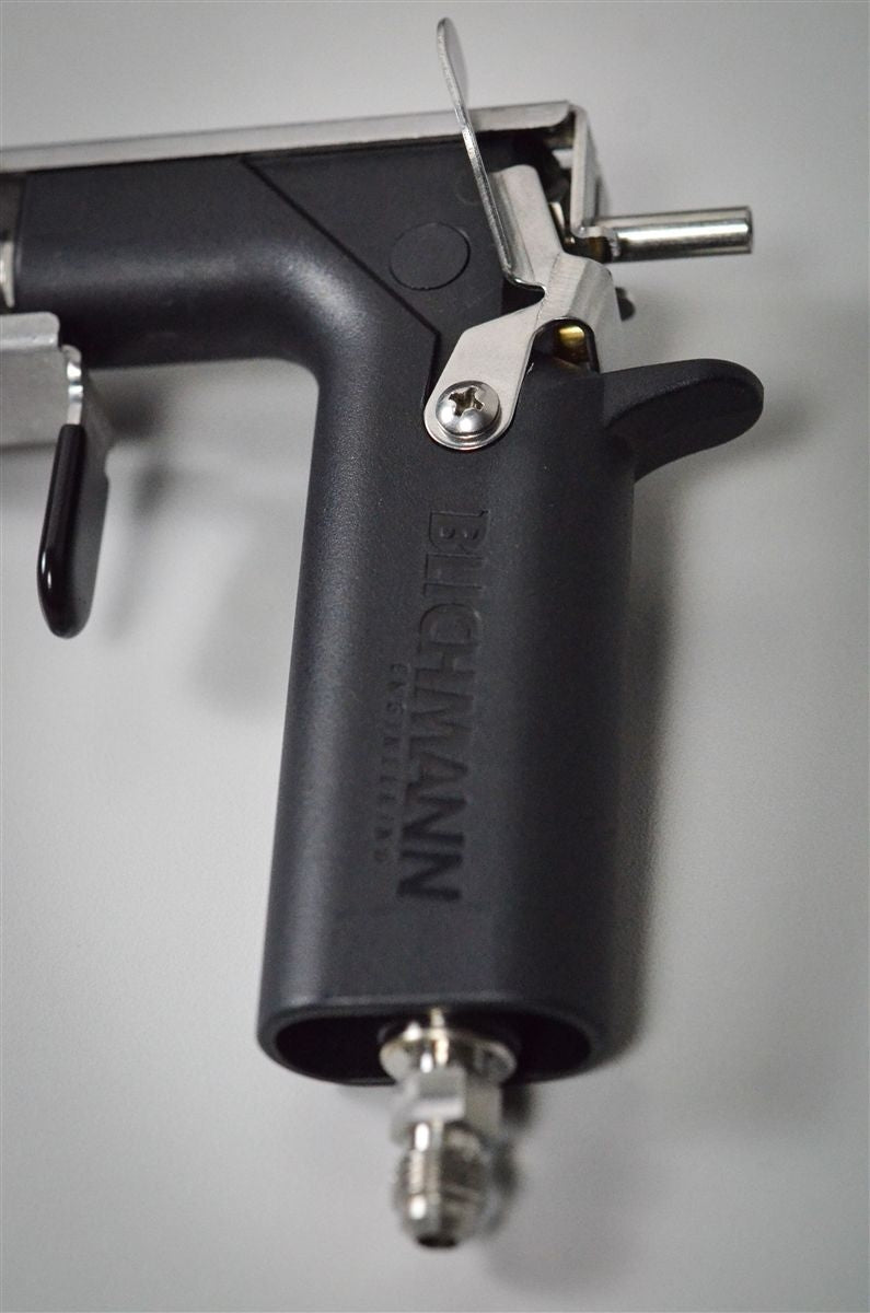 Et nærbilde av Blichmann BeerGun flaskefyller fra Blichmann ligger på en grå flate og viser avtrekkeren, munnstykket og tilkoblingsbeslagene.