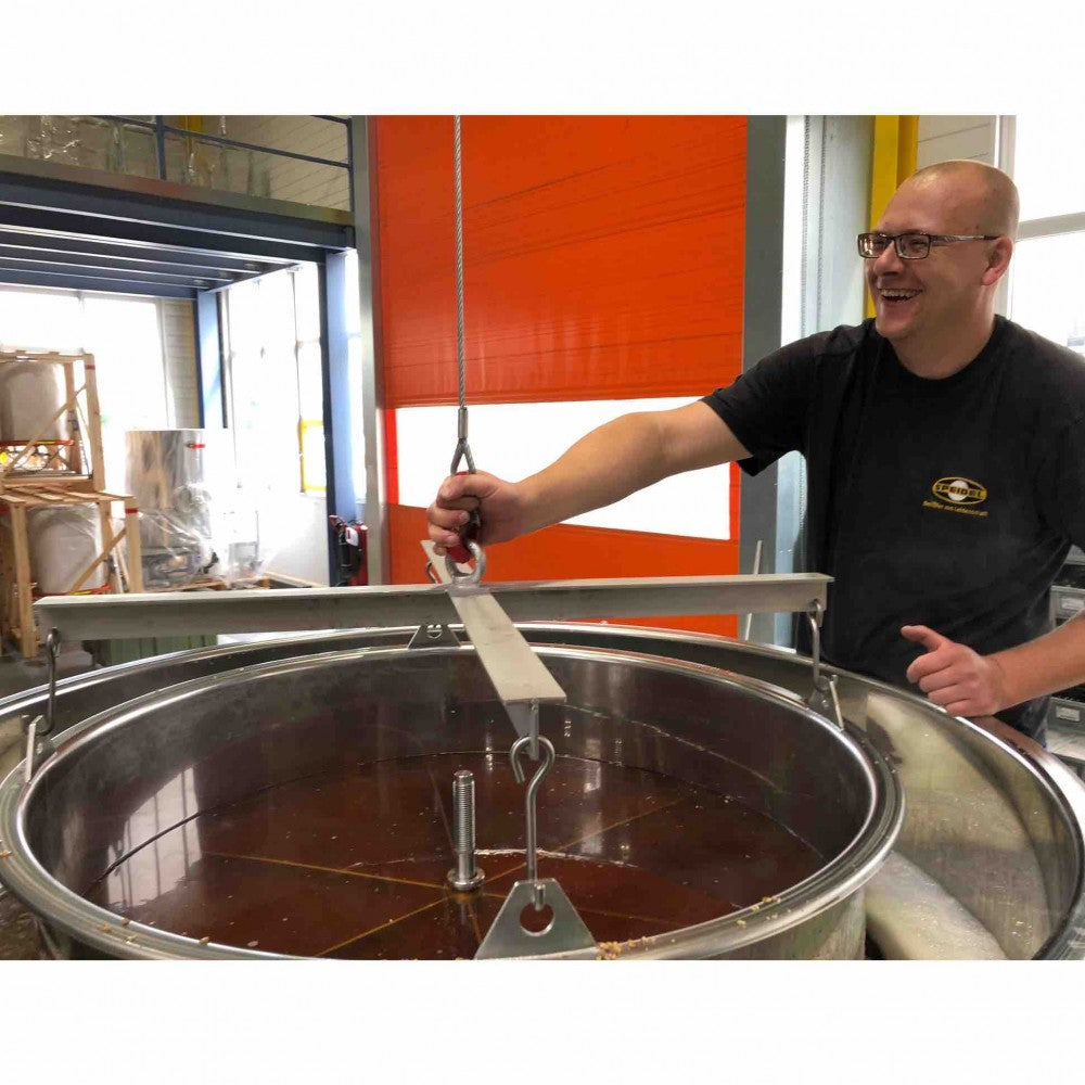 En person bruker et løfteverktøy i metall over en stor tank i rustfritt stål, en del av Speidel #Braumeister 1000L - Bestillingsvare by Speidel, inne i et industribryggeri for kommersiell ølproduksjon.