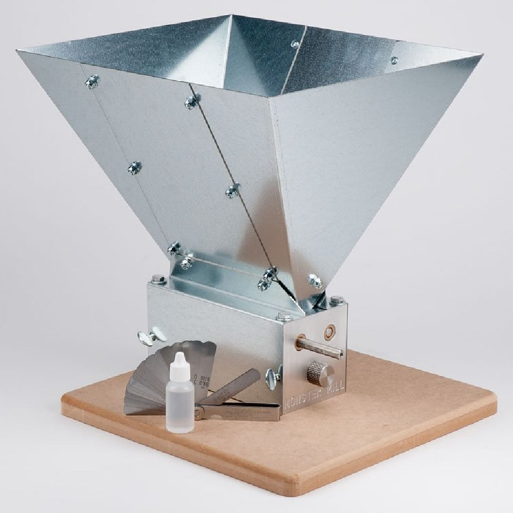 Monster Brewing Hardware Monster Mill MM-3, som har en solid metallkonstruksjon med base og trakter, vises for hjemmebrygging sammen med et vifteformet måleverktøy og en liten dråpeflaske i forgrunnen.