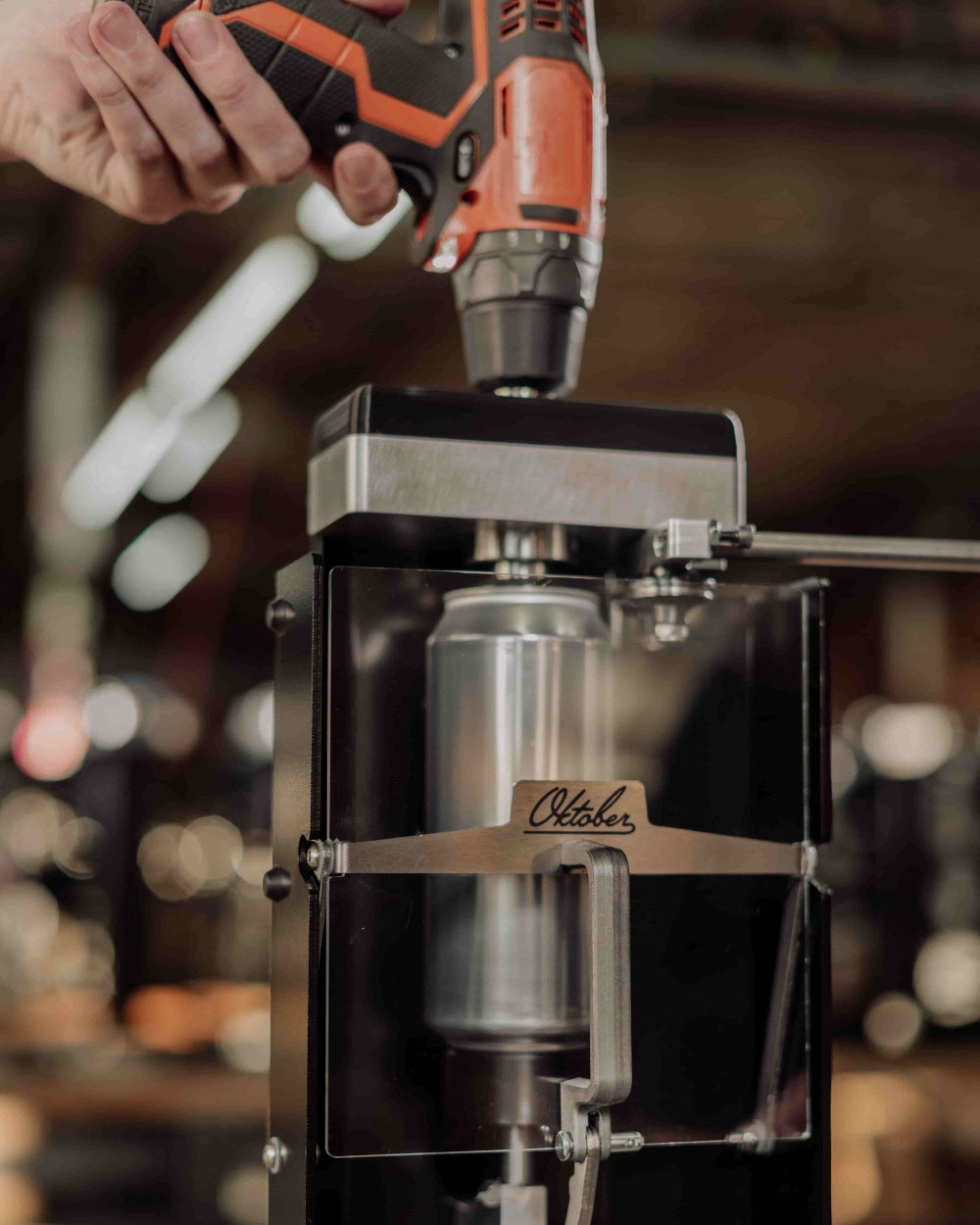 En person bruker BenchMK Drill-Powered Can Seamer fra Oktober Design til å forsegle en metallboks i et industrielt miljø for boksmaskin hjemmebryggere.