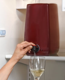 En hånd tapper hvitvin fra aPour Premium Wine Dispensing System fra Fermtech ned i et vinglass på en kjøleskapshylle.