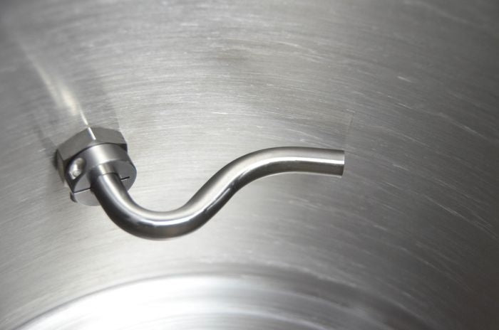 Nærbilde av Blichmann Kettle Whirlpool Kit med G2 Linear Flow Valve, som består av en rørkobling i rustfritt stål med bøyd tut og NPT-gjenger inne i en metallbeholder.