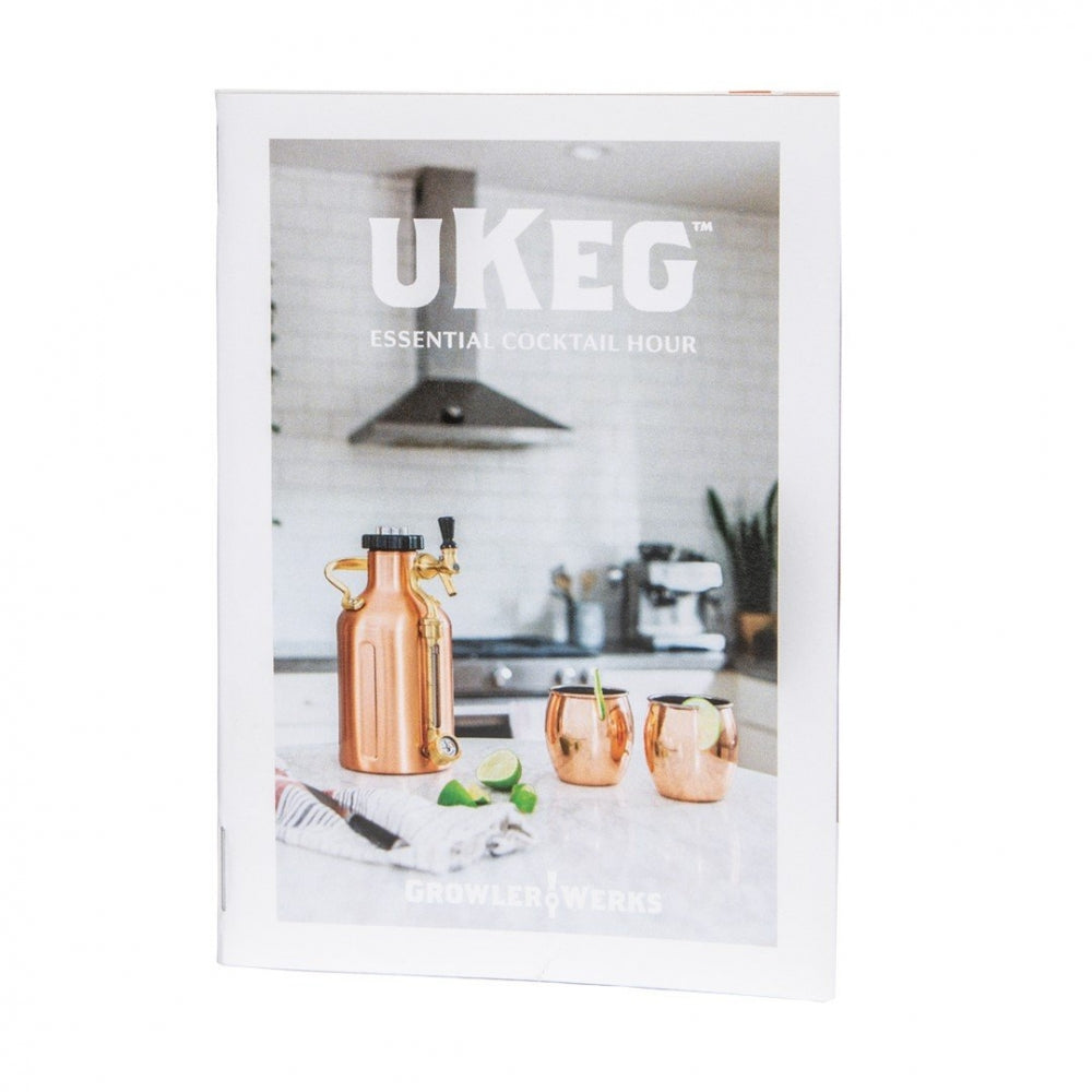 GrowlerWerks uKeg Cocktail Recipe Book er vist på en kjøkkenbenk sammen med en growler i kobber, to kobberkrus og limekiler.