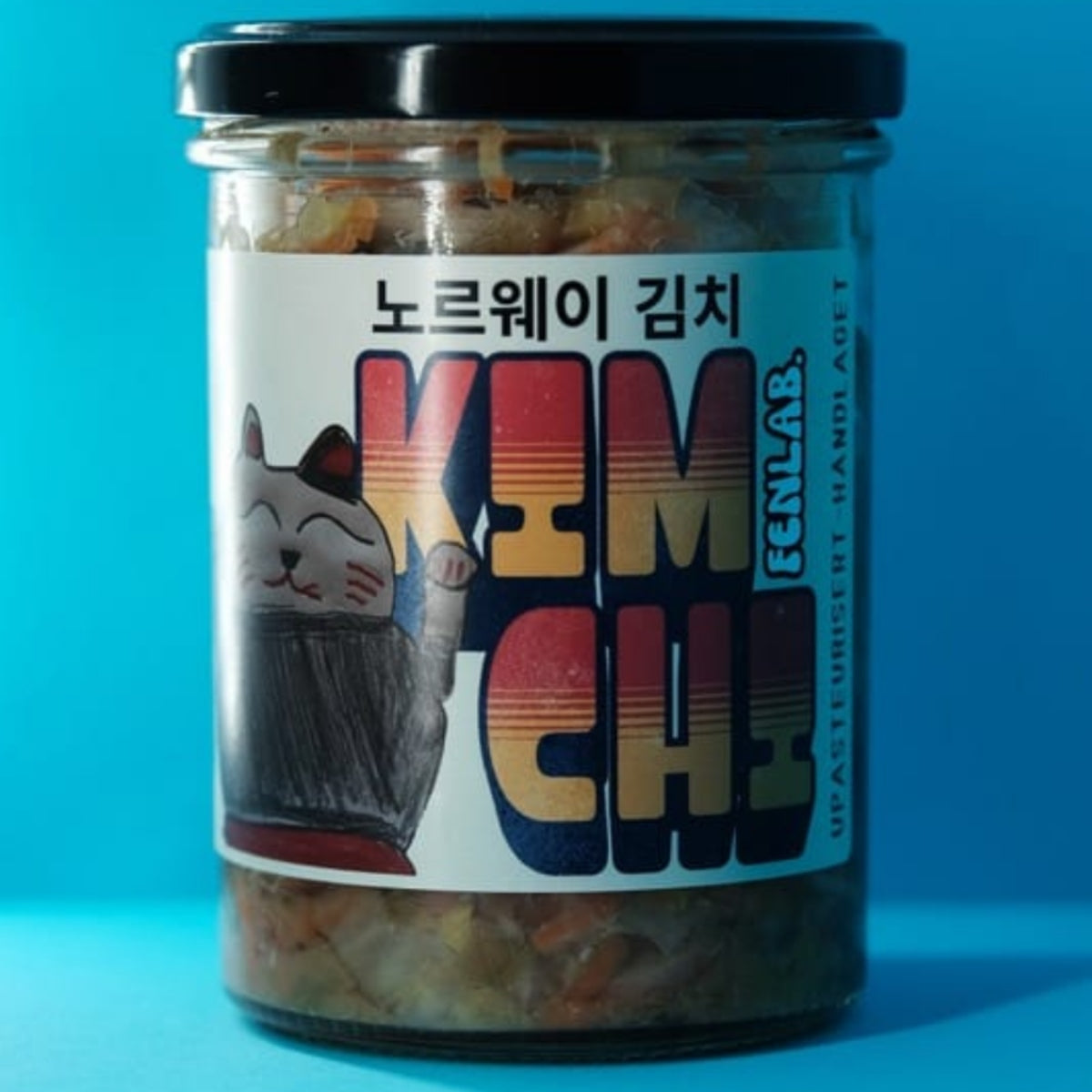 En glasskrukke på 435 ml med «Kimchi Upasteurisert» fra Fen Lab, med en tegneseriekatt og en iøynefallende, fargerik «KIMCHI»-tekst på engelsk og koreansk på etiketten, naturlig fermentert og produsert i Norge.