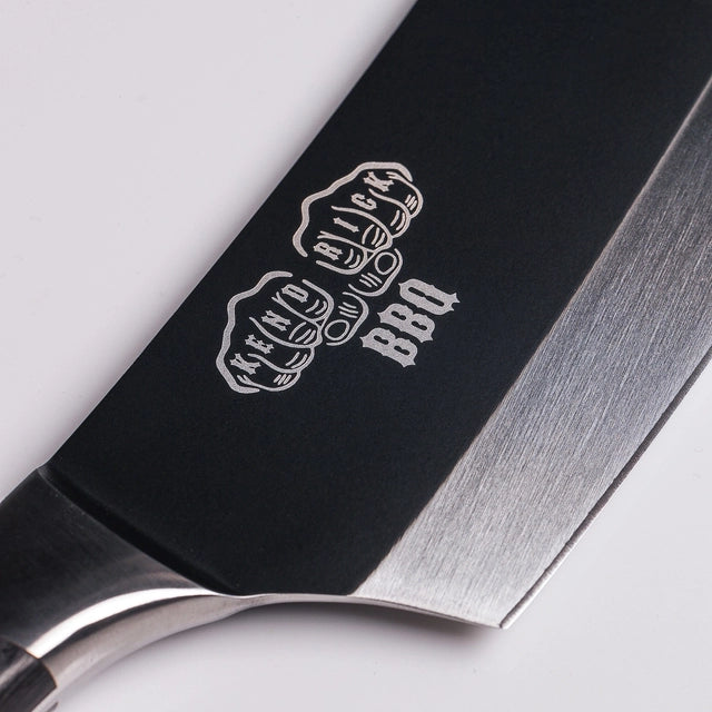 Nærbilde av Bennie Kendrick BBQ-kniven fra Messermeister, med "BBQ" og et messingknoke-design inngravert på bladet i tysk X50 rustfritt stål.