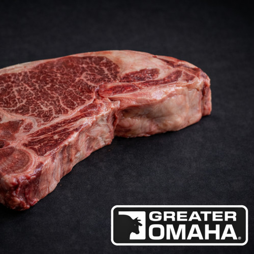 En Storfe T-Bone Greater Omaha 500g biff ligger på en svart overflate, med Greater Omaha-logoen i nedre høyre hjørne.