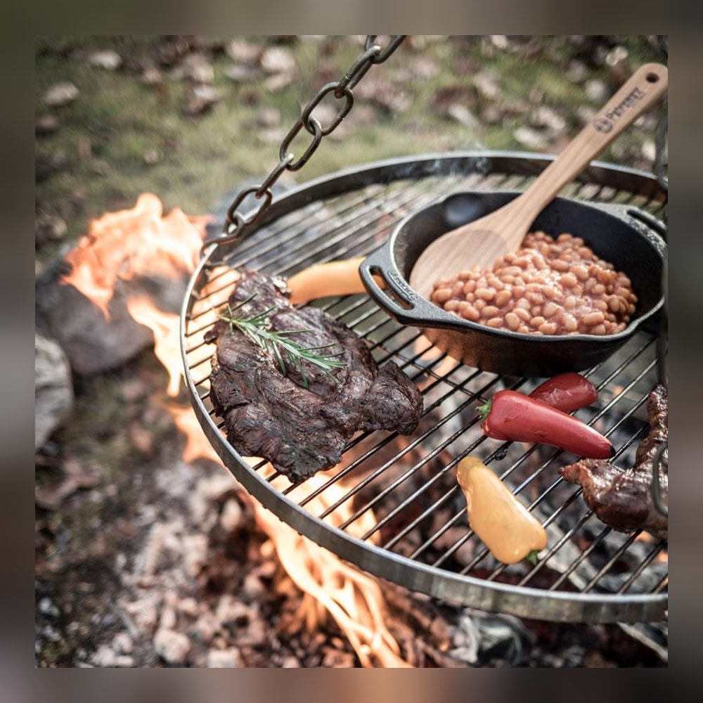 Kött, grönsaker och gjutjärnspanna på Petromax hängande grillgaller över elden