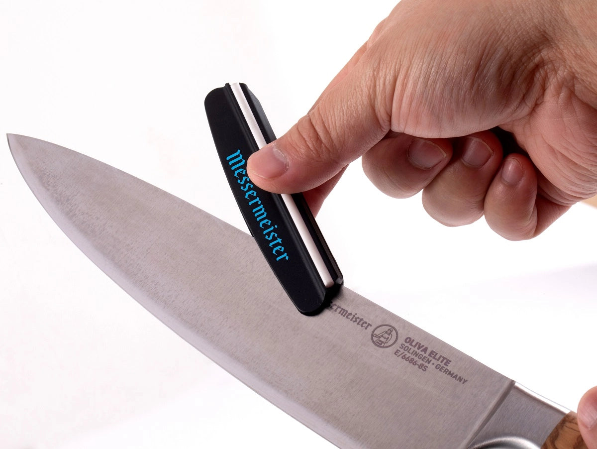 En hånd bruker Messermeister Vinkelguide For Kniv Sliping til å slipe et kjøkkenknivblad i en vinkel på 15°.