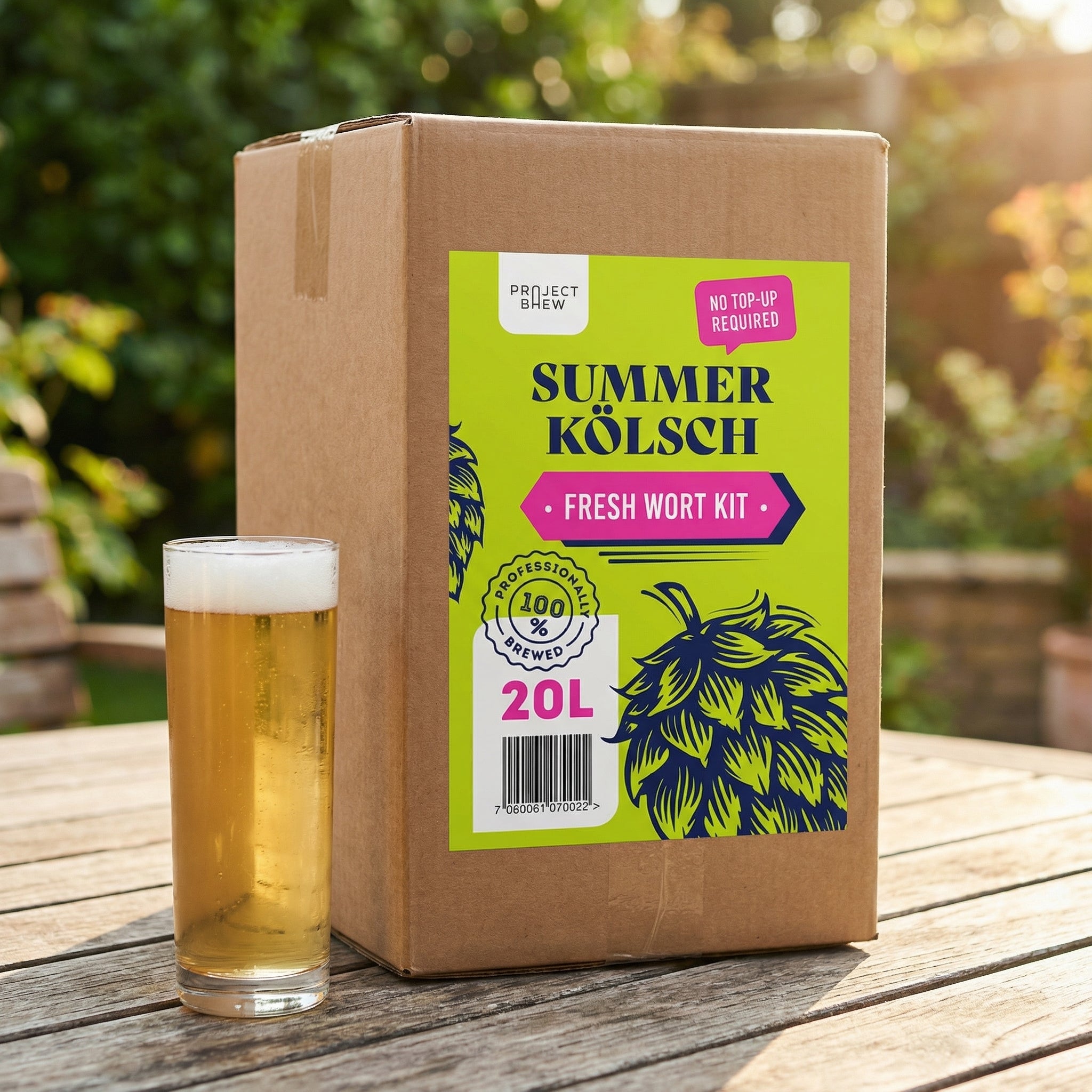 En pappeske merket Project Brew Summer Kölsch - 20L Fresh Wort Kit står på et bord utendørs ved siden av en halvliter lyst øl, og fremhever dette forfriskende fullkornssettet som passer perfekt til sommerbrygging.