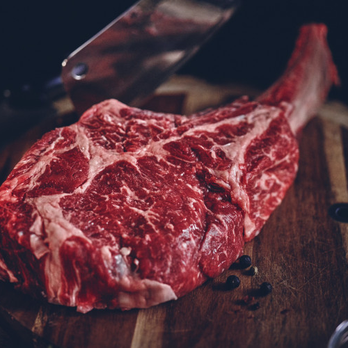 En Storfe Tomahawk Irland (Kr 550/kg, 1-1,5 kg per stykke) med synlig marmorering ligger på et skjærebrett i tre ved siden av en kjøttkniv.