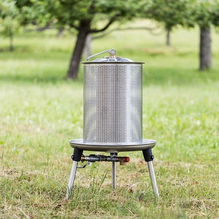 Speidel Hydropress 40L, en rustfritt stål fruktpresse fra Speidel, står på korte ben utendørs i gresset med trærne bak - ideelt for å presse eplejuice på en enkel måte.