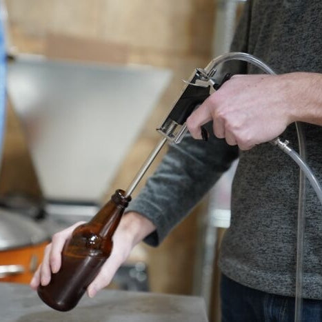 Noen bruker en Blichmann BeerGun flaskefyller med slange til å fylle en brun glassflaske, ideell for hjemmebrygging eller tapping av drikkevarer.