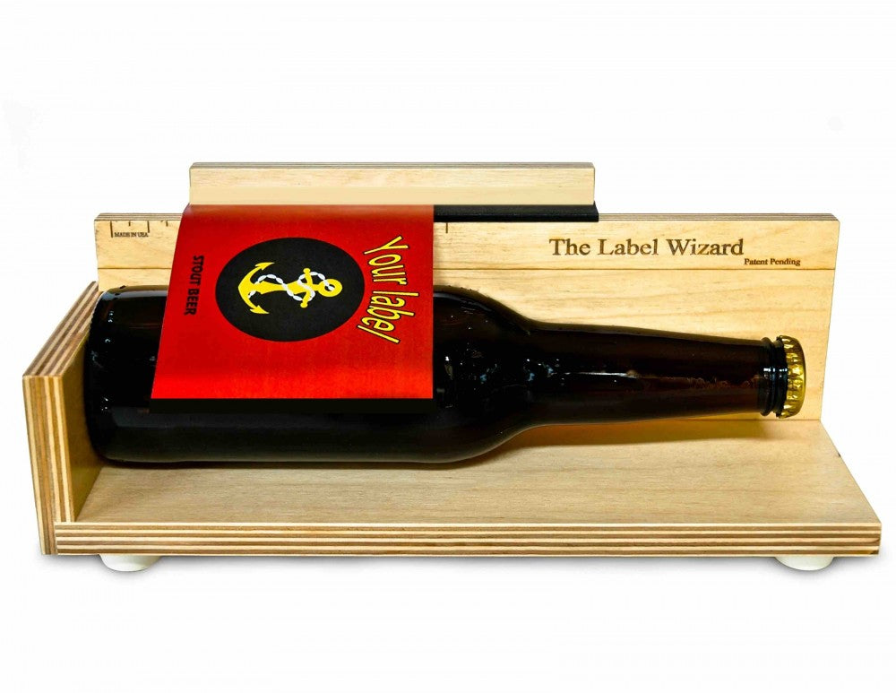 En brun ølflaske med rød etikett hviler i Label Wizards manual etikettmaskin-The Label Wizard, perfekt for hjemmebryggere som vil sette etiketter på flasker.