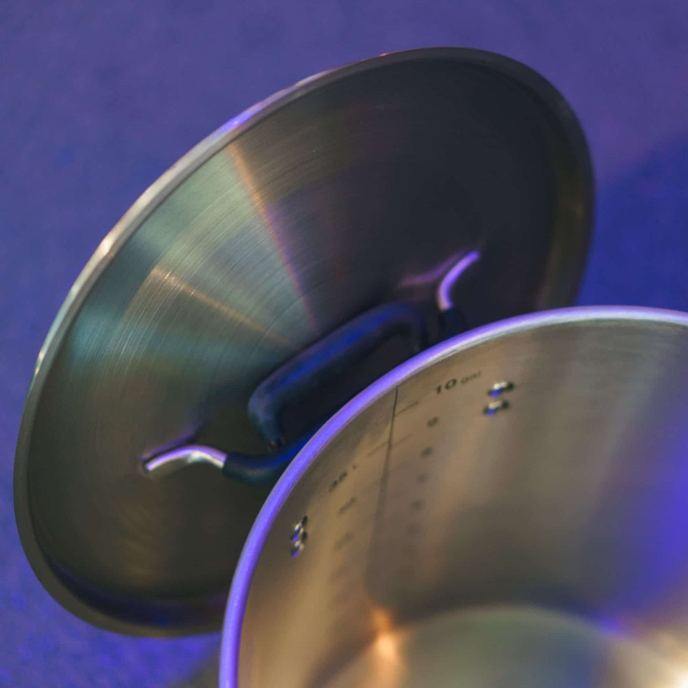 Nærbilde av Ss Brewtech Ss TC Brew Kettle 189L (50 gal) Bryggekjele med tri-clamp-port, lokket delvis åpent for å avsløre innvendige målmarkeringer, opplyst av blå og lilla belysning.
