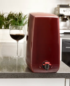 Fermtech aPour Premium Wine Dispensing System står på kjøkkenbenken ved siden av et glass fylt med rødvin.