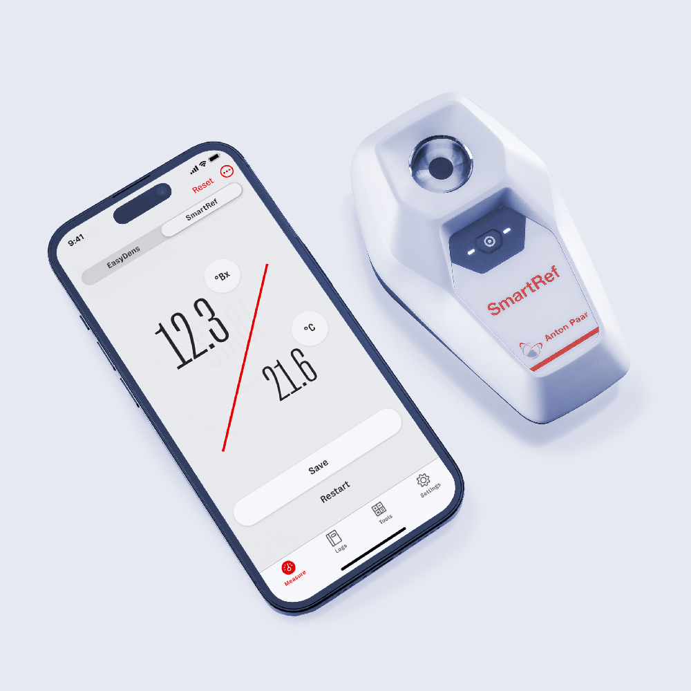 En smarttelefon viser måledata ved siden av Anton Paar SmartRef Digitalt Refraktometer, som er ideelt for ølbrygging og presis vørter- og alkoholkorreksjon, på en lys bakgrunn.