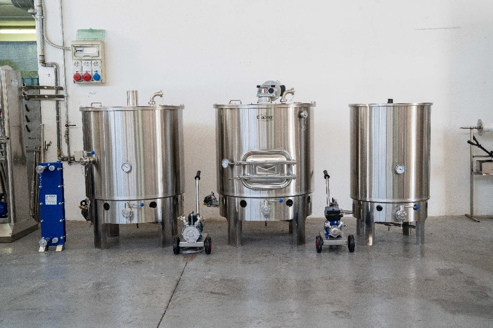 Tre store EnoBeer Enobrau 500 Professional Flame-bryggertanker i rustfritt stål med målere og pumper står side om side i et industrielt miljø, med det avanserte EnoBrew-Touch-panelet for presis kontroll.