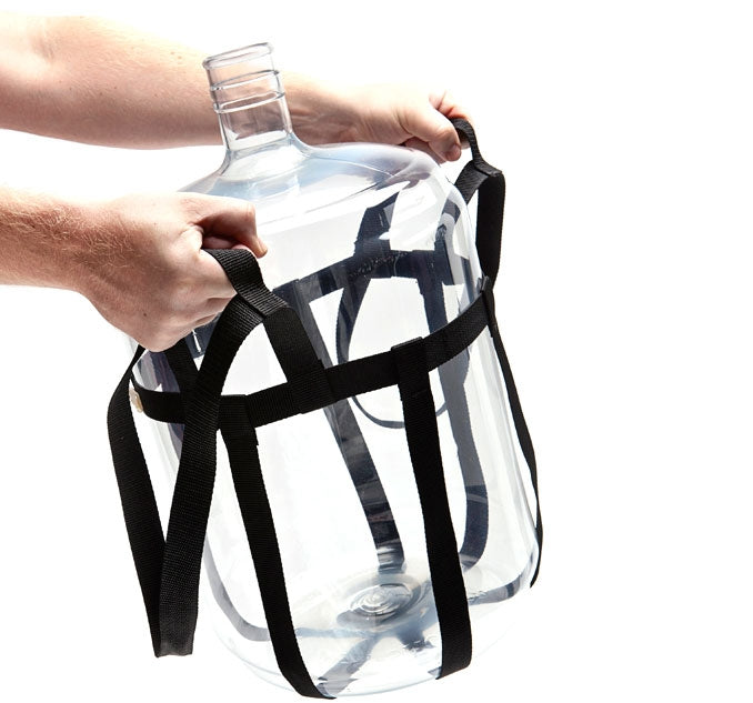 En person holder en stor, tom glassflaske med The Vintage Shop's Carboy Carrier - løftestropper til gjæringskar sele mot en hvit bakgrunn.