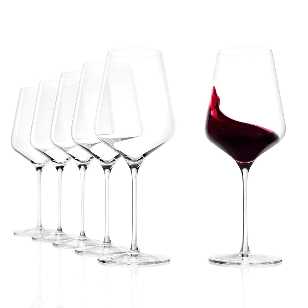 Seks STARlight Bordeaux vinglass 675 ml fra Stölzle Lausits står på rekke og rad; fem er tomme, mens ett klart krystallglass fanger opp rødvinen midt i spruten.